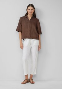 Chemise en lin marron à manches courtes avec col et fermeture à boutons, associée à un pantalon en lin blanc et des sandales beiges avec un design de bride tressée.
