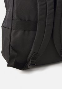 Schwarzer Rucksack aus strukturiertem Stoff, mit gepolsterten Trägern, Seitentaschen und verstellbaren Schnallen zur Sicherung von Gegenständen. Schlichtes, funktionales Design.