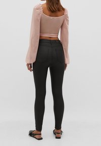 Zwarte skinny jeans met een hoge taille, gecombineerd met een lichtroze getailleerd langemouwen shirt met pofmouwen en een cropped snit.