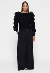 Zwarte gebreide trui met geraffineerde tule mouwen, in combinatie met hoge zwarte wijde broek met een riemdetails bij de taille.