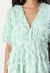 Mint green dress made of soft fabric, featuring a textured design with fringing, V-neckline, and short sleeves. Elastic waist detail.