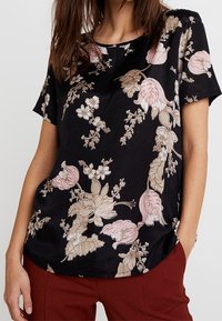 Haut noir à manches courtes avec des motifs floraux dans les tons rose et beige. Tissu doux, coupe décontractée et encolure ronde. Ourlet légèrement incurvé.