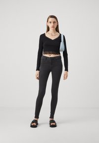 Svart langermet crop topp med blondekanter, parret med mørke slanke jeans og kraftige svarte sandaler. Blå veske og perlekjede inkludert.