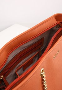Borsa tote in pelle arancione con una superficie texture, dotata di una tasca con zip e diversi slot per carte all'interno. Finiture in oro.
