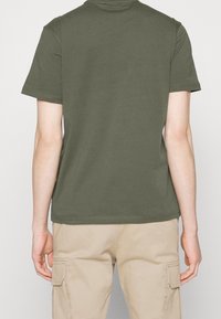 Oliven grøn bomulds-t-shirt med rund halsudskæring, korte ærmer og pæn syning, kombineret med khaki cargobukser. Enkel, afslappet design.