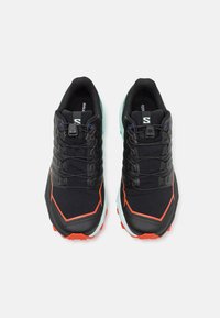 Zapatillas de correr negras con una parte superior texturizada, que presentan acentos naranjas, un sistema de cordones seguro y una suela de color turquesa contrastante.