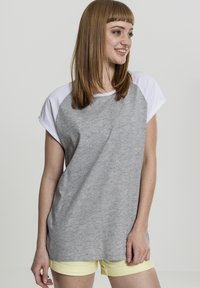 Grå kortærmet t-shirt med hvide raglanærmer, lavet af blødt stof. Har en afslappet pasform og en rund halsudskæring. Kombineret med gule shorts.