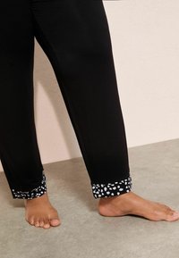 Pantaloni negri cu un tiv alb patterned la mansete, realizați dintr-un material neted. Au o croială lejeră și un design drept.