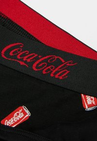 Schwarze Baumwollunterwäsche mit rotem Bund, der das "Coca-Cola"-Logo in Schreibschrift trägt. Rote Akzente beinhalten einen kleinen Druck einer Coca-Cola-Dose.