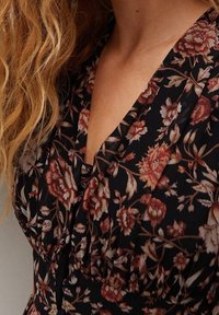 Blumenmuster Kleid mit schwarzem Hintergrund, verziert mit roten und cremefarbenen Blumen, einem V-Ausschnitt und sanften Falten um den Ausschnitt.