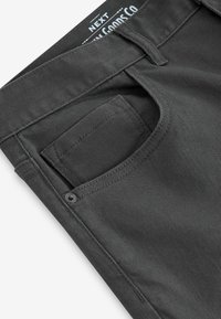 Grå denim bukser med en tekstureret overflade, der har en frontlomme, bæltestropper og en knaplukning ved taljen.