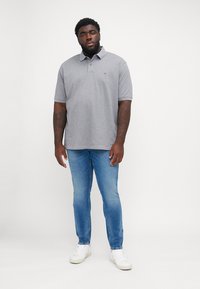 Cămașă polo gri cu mâneci scurte și guler, asortată cu blugi din denim bleu deschis și adidași albi. Design simplu și croială lejeră.