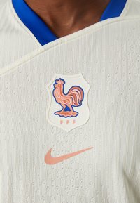 Biely textúrovaný dres s modrým golierom. Obsahuje erb s kohútom a "FFF" v ružovej farbe, spolu s ružovým logom Nike.