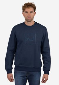 Sudadera azul marino hecha de tela suave, con un logo cuadrado con diseño "AJ" en un azul ligeramente más claro, puños y dobladillo acanalados.