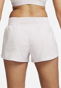 Pantalones cortos deportivos de color rosa claro con una cintura elástica fruncida, tela suave y detalles de costura sutiles. La vista trasera muestra una cobertura mínima de las piernas.