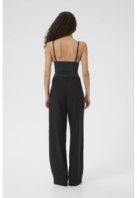 Pantalon noir à jambes larges avec une texture lisse, taille haute et poche arrière. Associé à un haut noir ajusté à fines bretelles.