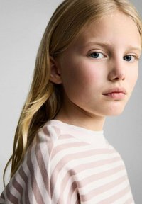 Pullover a righe rosa chiaro e crema con scollatura rotonda; il modello ha i capelli lunghi biondi e occhi blu, illuminato dolcemente su uno sfondo neutro.