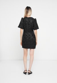 Čierne krátke šaty s nafúknutými rukávmi, ktoré majú textúrované kvetinové vzory. Ukončené skrytým zipsom na zadnej strane a priliehavým strihom.