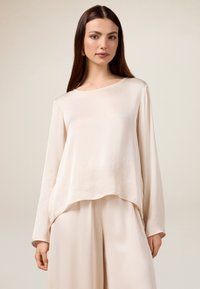 Helles beige Langarmoberteil mit einem lockeren, fließenden Design, Rundhalsauschnitt und weichem Material, kombiniert mit passenden weiten Hosen.
