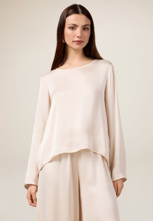 Helles beige Langarmoberteil mit einem lockeren, fließenden Design, Rundhalsauschnitt und weichem Material, kombiniert mit passenden weiten Hosen.