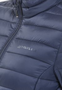 Marinblå puffjacka med horisontell quiltning, hög krage, frontdragkedja och "WHISTLER"-logotyp i reflekterande finish på bröstet.