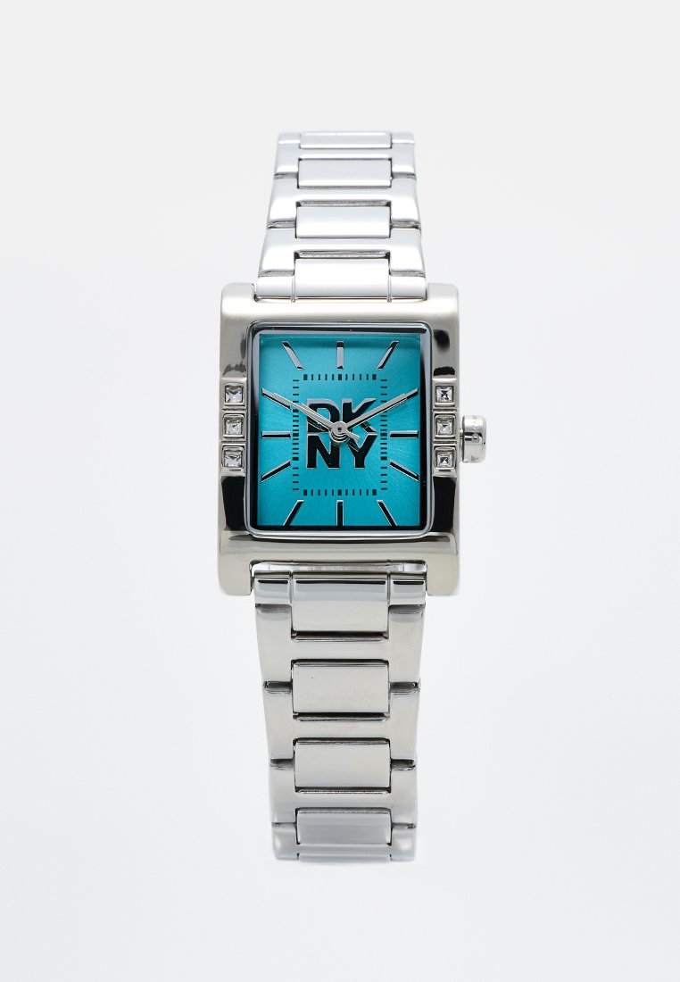 Quadratische silberne Uhr mit einem glänzenden türkisfarbenen Zifferblatt, schwarzem Logo, silbernen Stundenmarkierungen und Kristallakzenten am Gehäuse. Armband aus rostfreiem Stahl.