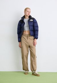 Tengeri kék puffernadrág fekete akcentusokkal, szürke crop top, bézs cargo nadrág és zöld tornacipő krémszínes csíkokkal; texturált felületek és látható cipzárak.