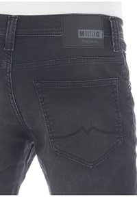 Vaqueros de mezclilla negros con un bolsillo trasero que presenta un diseño de costura curvada y una etiqueta rectangular de la marca que dice "Mustang True Denim".