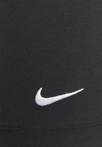 Tessuto atletico nero con texture a coste. Presenta un logo Nike ricamato bianco e dettagli di cucitura sottili vicino all'orlo.