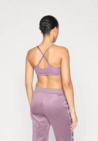 Μωβ αθλητικό σουτιέν με λουράκια που διασταυρώνονται και άνοιγμα στην πλάτη. Το ύφασμα είναι λείο και ελαστικό, σε συνδυασμό με παντελόνι που ταιριάζει.