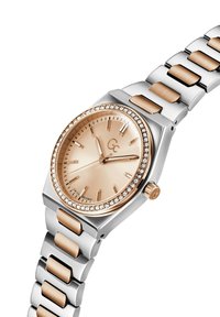 Klocka i rostfritt stål med fyrkantig klockkåpa, roséguld accenter och en bezel prydd med kristaller. Ljust rosa urtavla med radial textur och timmarkeringar.