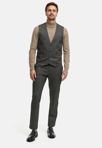 Grå uldsvest med fem knapper, parret med en beige turtleneck og matchende skræddersyede bukser. Sorte loafers fuldender outfittet.