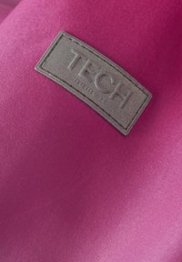 Rosa Textil mit glatter Oberfläche, ausgestattet mit einem grauen rechteckigen Etikett, das mit "TECH" geprägt ist, und einer Naht entlang der Kanten.
