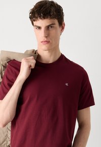 Bordeaux bomulds t-shirt med rund hals og korte ærmer, med et lille broderet logo på venstre bryst; glat overflade.