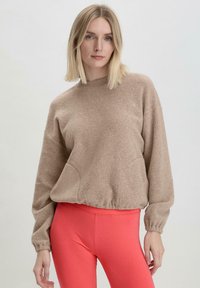 Beige Fleece-Sweatshirt mit geripptem Halsausschnitt und Bündchen, mit überschnittenen Schultern und lockerer Passform; kombiniert mit leuchtend korallenfarbenen Leggings.