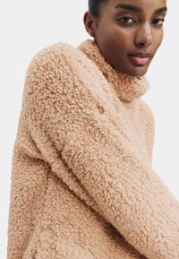 Beige, blød sweater med høj krave og lange ærmer. Blød tekstur, løs pasform, med et hyggeligt, blødt udseende.