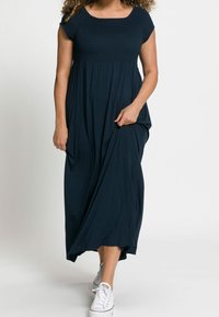 Marinblå maxiklänning med smockad byst och korta ärmar, med en flödande A-linjekjol och bärs med vita sneakers.