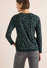 Langärmliger Pullover in Dunkelgrün mit einem schwarzen Leopardenmuster. Verfügt über einen runden Ausschnitt und Saum mit navyblauen Rippdetails.