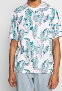 Kortärmad skjorta i lätt material, med vit bakgrund och gröna och rosa bladmönster. Klassisk krage och knappframsidan.