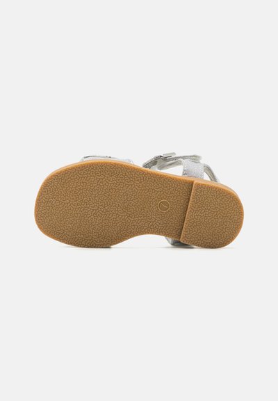 Vue inférieure d'une sandale argentée, présentant une semelle en caoutchouc texturé avec des nervures et de couleur beige, maintenue par des sangles ajustables.