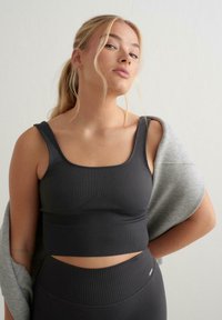 Grå ribbet crop top med brede stropper, med en tettsittende design og teksturert stoff. En lys grå hettegenser som henger over den ene skulderen.