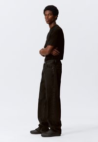 Black t-shirt, loose-fitting black denim pants, and black textured shoes. Simple design with no visible patterns or hardware details.