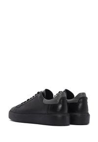 Un paio di sneakers in pelle nera a basso profilo con inserti grigi sul tallone e suole di gomma spesse, mostrate da una vista angolata posteriore su sfondo bianco.