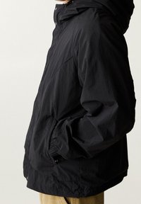 Giubbotto leggero nero con cappuccio, caratterizzato da una trama sottile, polsini elasticizzati e chiusure a pressione. Design semplice e funzionale.