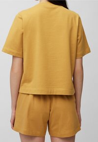 Camiseta de algodón amarilla con escote redondo, mangas cortas y un ajuste relajado, combinada con pantalones cortos amarillos a juego, ambos con costuras limpias.