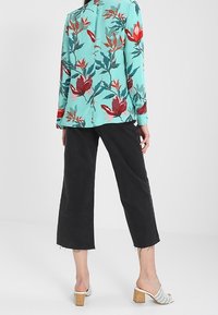 Miętowa kurtka w kwiatowy wzór z długimi rękawami, zestawiona z czarnymi spodniami 3/4 z postrzępionymi brzegami oraz białymi sandałami na obcasie typu block heel.