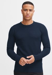 Navy blue knit sweater with a textured pattern, ribbed crew neckline, and cuffs. Fitted design, long sleeves, and subtle brand detailing at the hem.