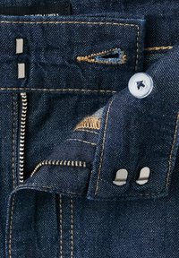 Detail of dark blue denim jeans showing zipper, button, and metal hooks with orange stitching.