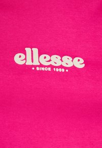 Roza pamučna tkanina s upečatljivim bijelim logotipom "ellesse" i natpisom "SINCE 1959" u jednostavnom sans-serif fontu.