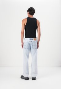 Zwarte mouwloze tanktop gedragen met lichtblauwe, loszittende jeans met achterzakken en een label op de tailleband. Zwarte schoenen.